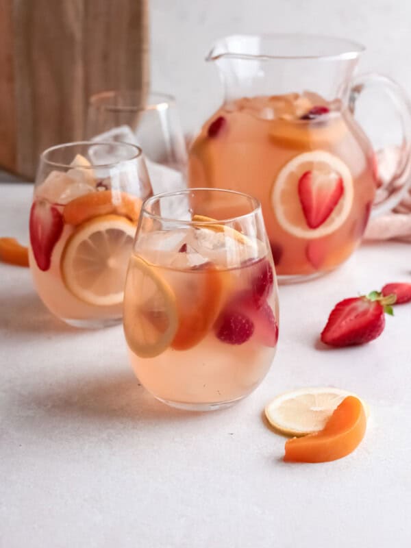 three-quarters view of 2 glasses of rose sangria in front of a pitcher.