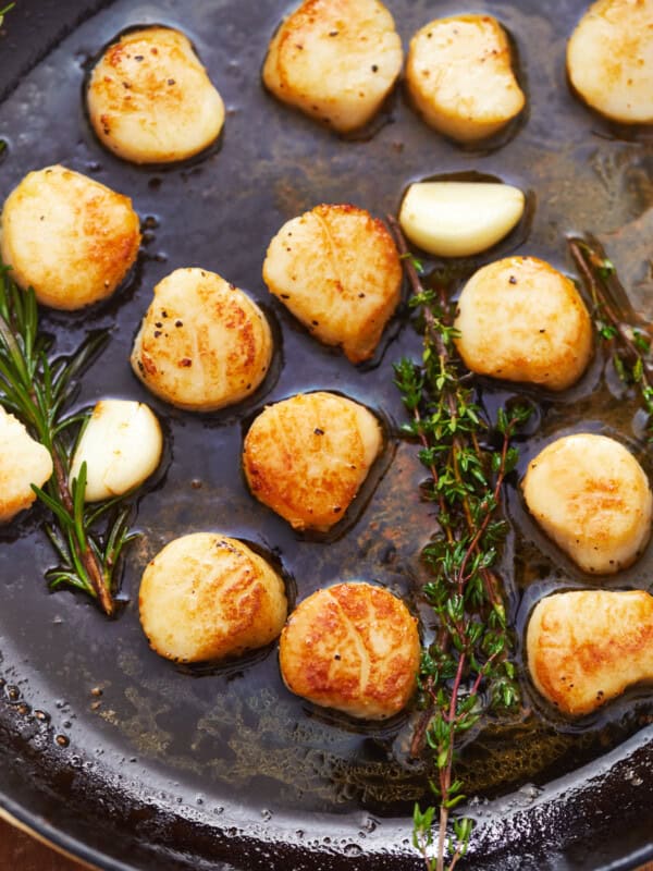 overhead view of seared scallops in a cast iron pan with herbs.