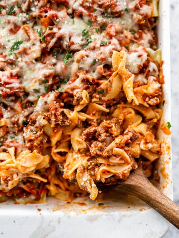 three-quarters view of the lower right corner of a sour cream noodle casserole with a wooden spoon.