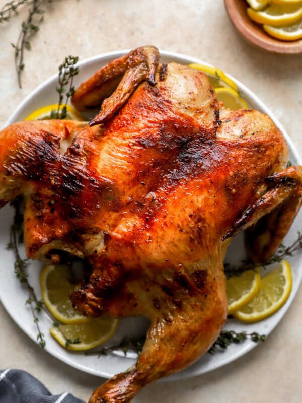 spatchcock chicken on a white plate with lemon slices.