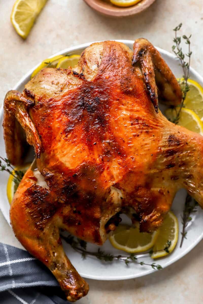 spatchcock chicken on a white plate with lemon slices.