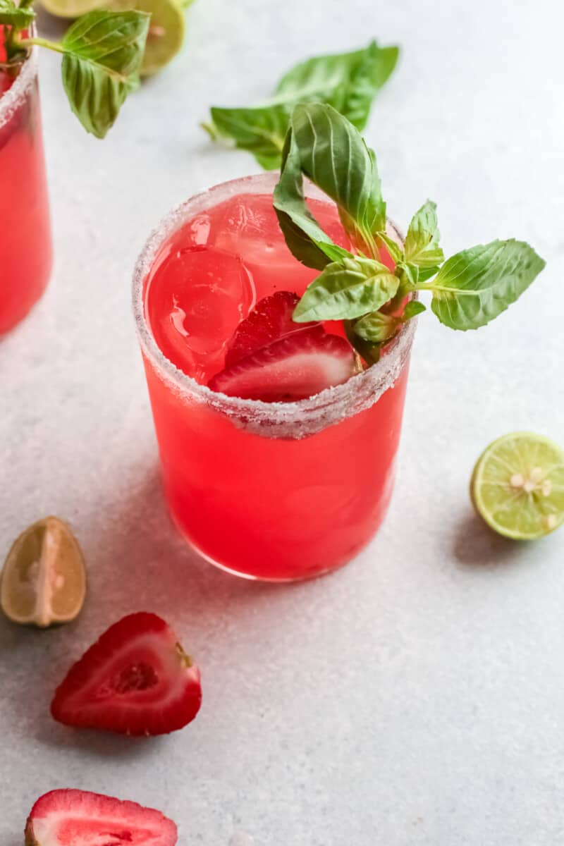 three-quarters view of a strawberry basil margarita garnished with basil and strawberries.