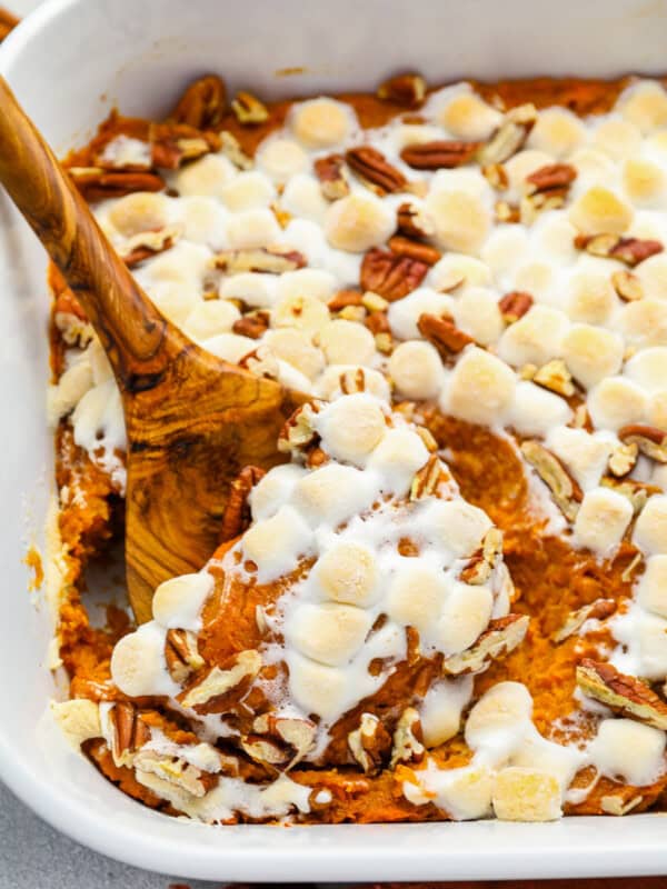 a wooden spoon scooping sweet potato casserole from a white rectangular baking dish.