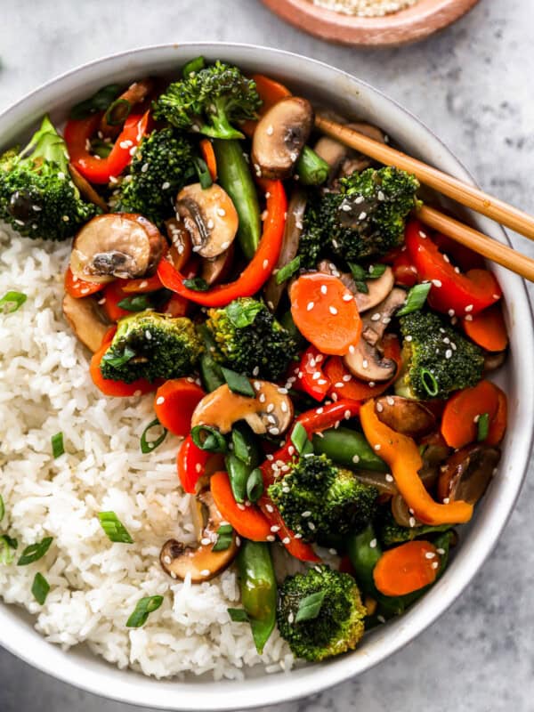 partial overhead view of vegetable stir fry in a white bowl with white rice and chopsticks.