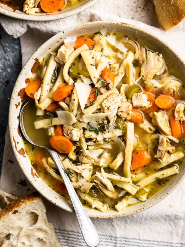 overhead view of a serving of chicken noodle soup in a white bowl with a spoon.