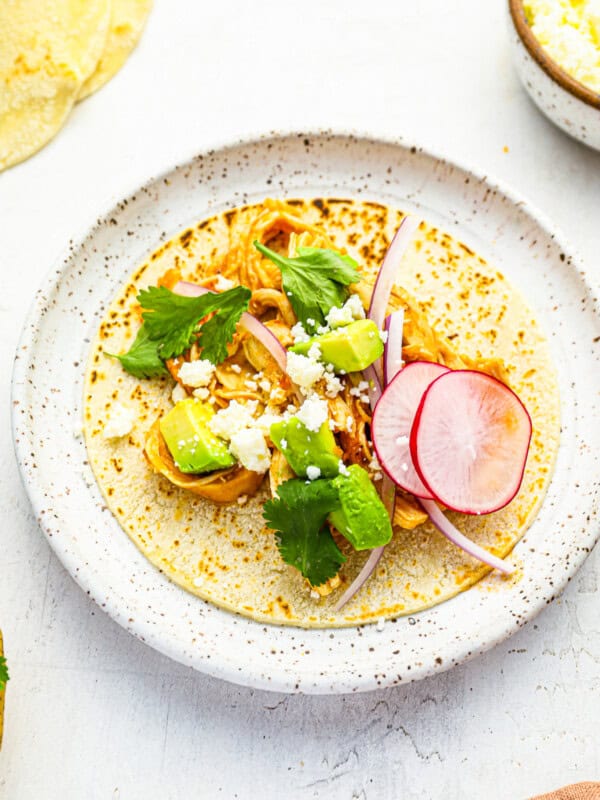 three-quarters view of a chicken tinga taco laid flat on a speckled white plate.