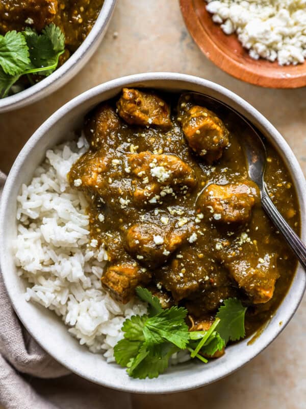 overhead view of a serving of chile verde in a white bowl with white rice, cilantro, and a fork.