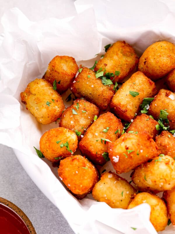 three-quarters view of tater tots in a parchment-lined serving dish topped with parsley.