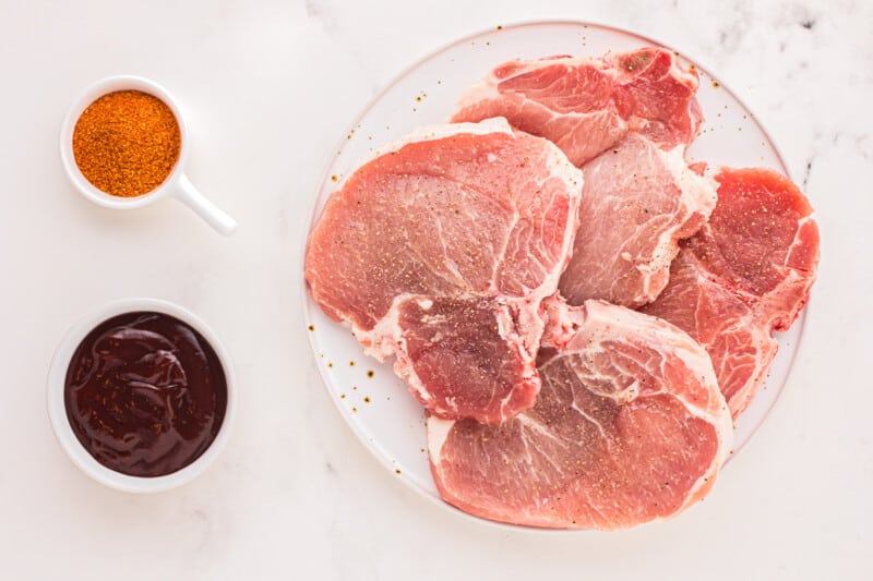 overhead view of 4 raw pork chops on a white plate.