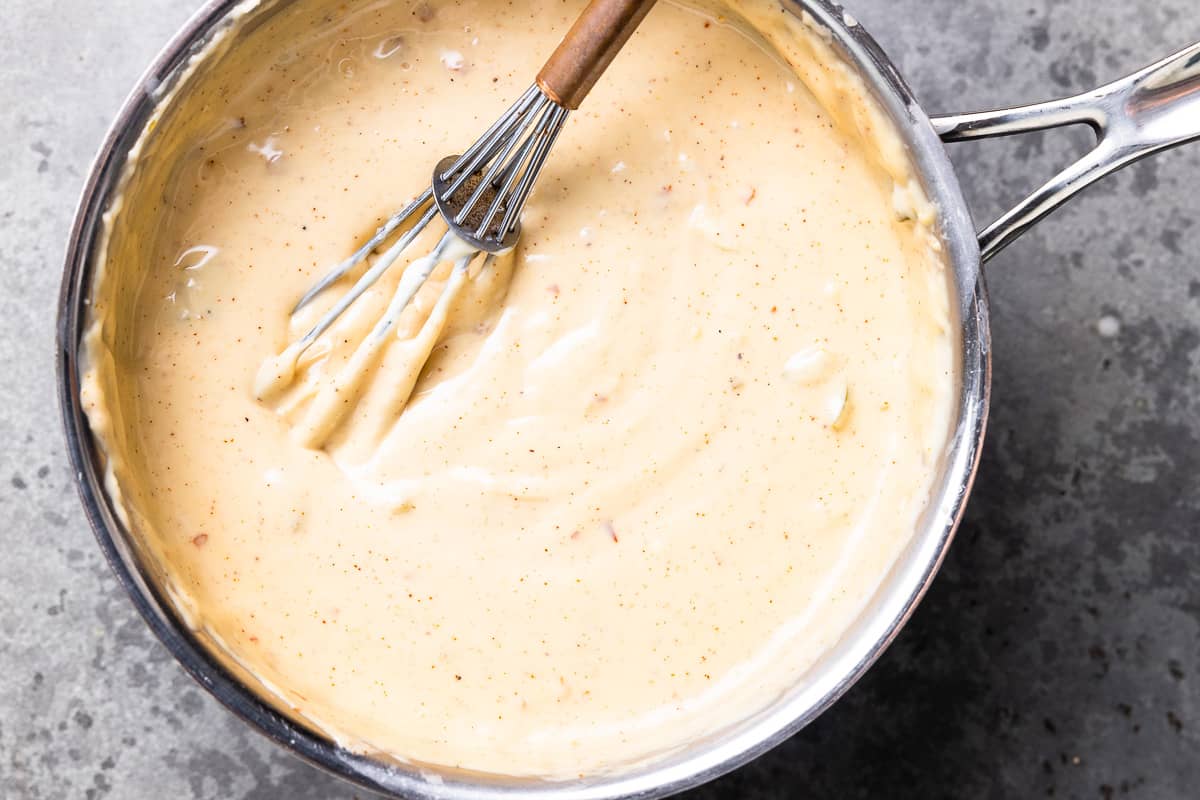 thickened white queso in a saucepan with a whisk.