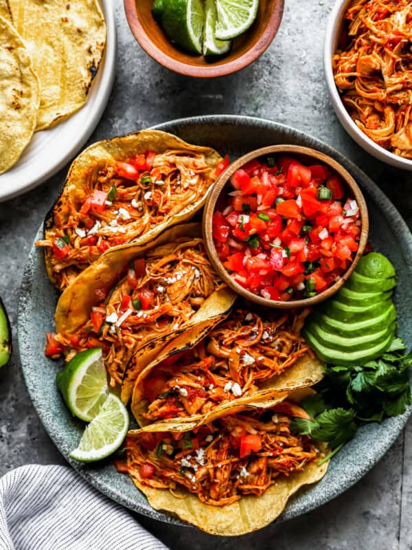 overhead view of 4 instant pot chicken tacos on a gray plate with salsa, avocados, and lime wedges.