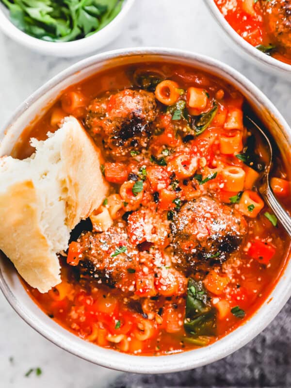 overhead view of a serving of meatball soup in a white bowl with a spoon and a piece of bread.