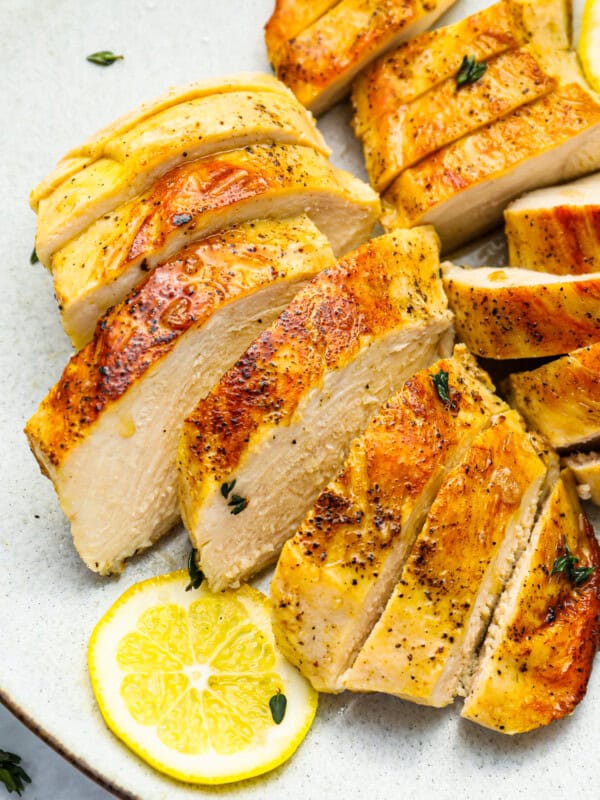 three-quarters view of 2 sliced sous vide chicken breasts on a white plate with a lemon slice.