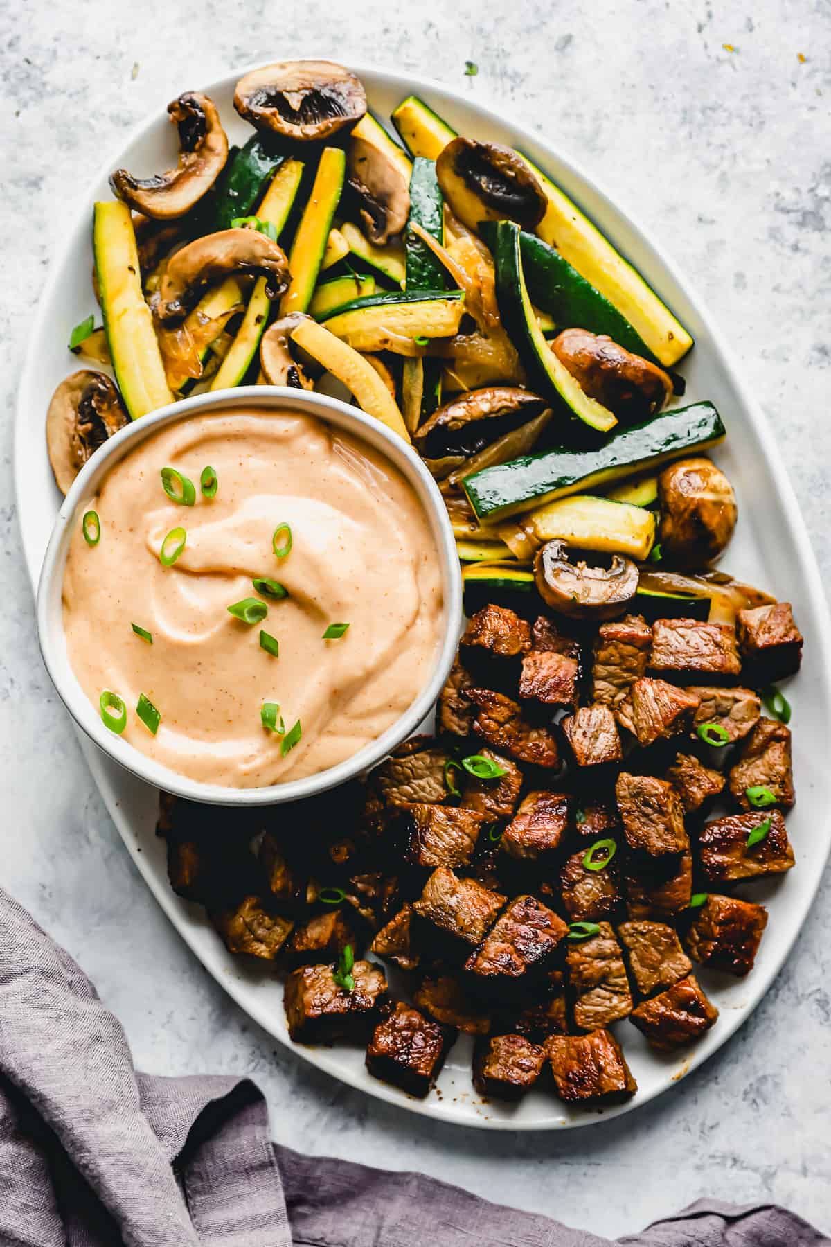 overhead view of homemade yum yum sauce in a white bowl on a platter with cubed steak and vegetables.