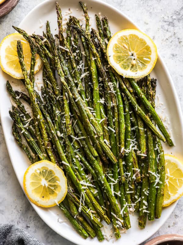 overhead view of air fryer asparagus on a white oval serving platter with lemon slices.