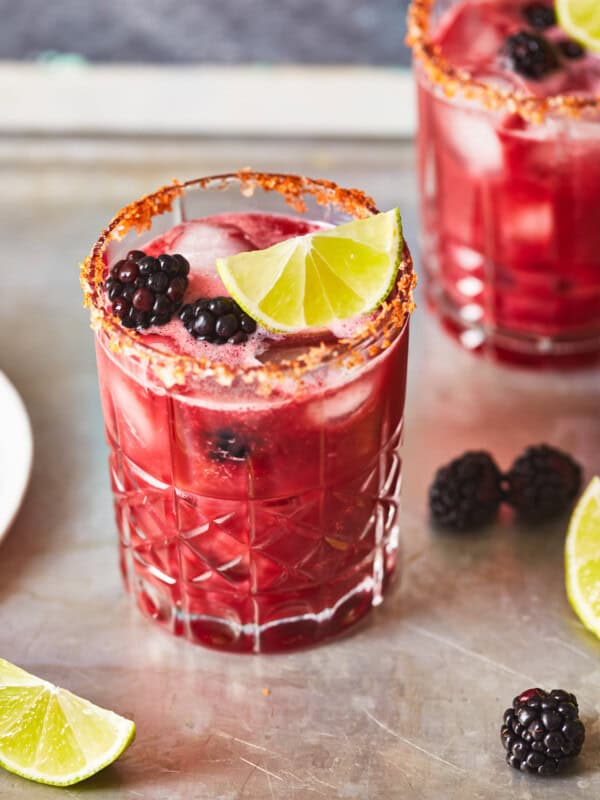 three-quarters view of a blackberry margarita in a short glass with a chili salt rim and blackberry and lime wedge garnish.