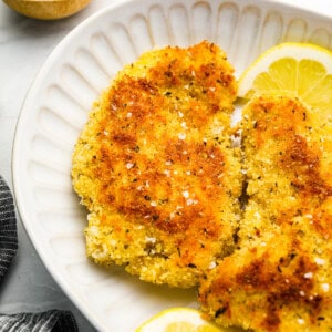 fried chicken breasts on a white plate with lemon wedges.