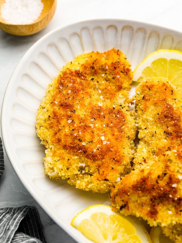 fried chicken breasts on a white plate with lemon wedges.