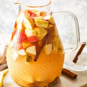 a pitcher of apple sangria with cinnamon sticks and apples.