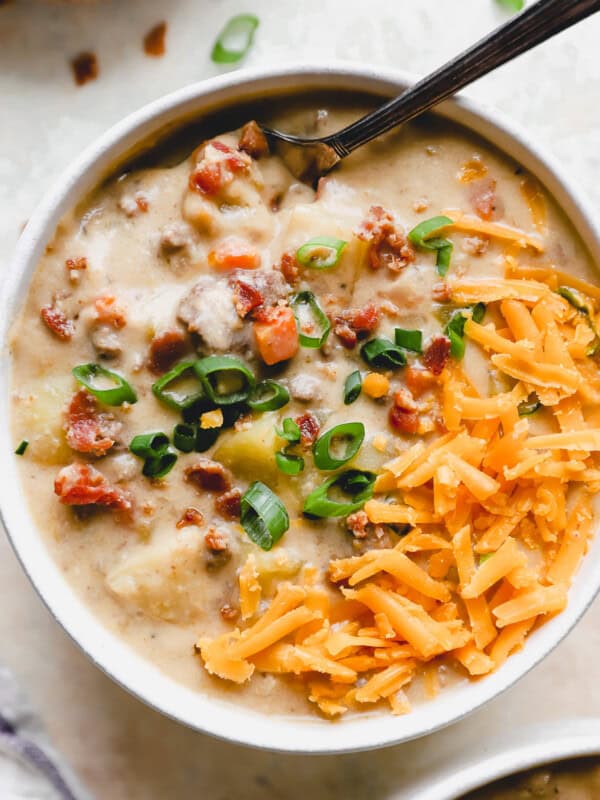 overhead view of a serving of cheeseburger soup in a white bowl with a spoon topped with bacon, green onion, and shredded cheese.