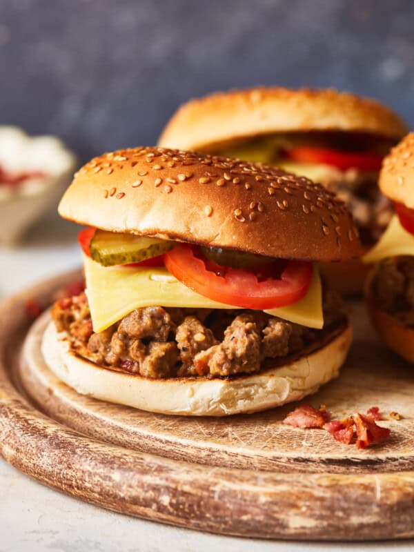 side view of crockpot cheeseburgers on a round wooden cutting board.