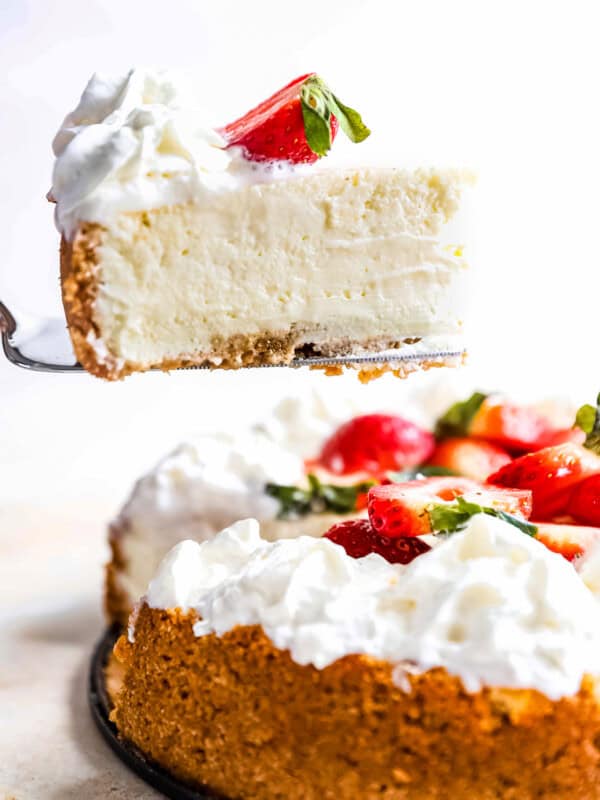 side view of a slice of easy cheesecake being lifted on a cake server from a whole cheesecake.