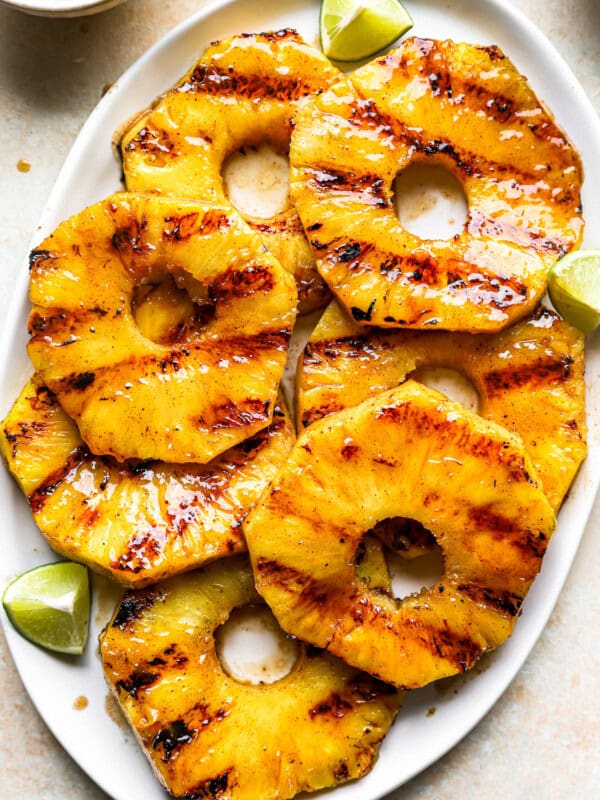 overhead view of slices of grilled pineapple on a white oval serving platter with lime wedges.