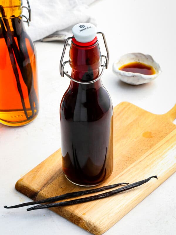 a bottle of homemade vanilla extract on a wooden cutting board with 2 vanilla bean pods.