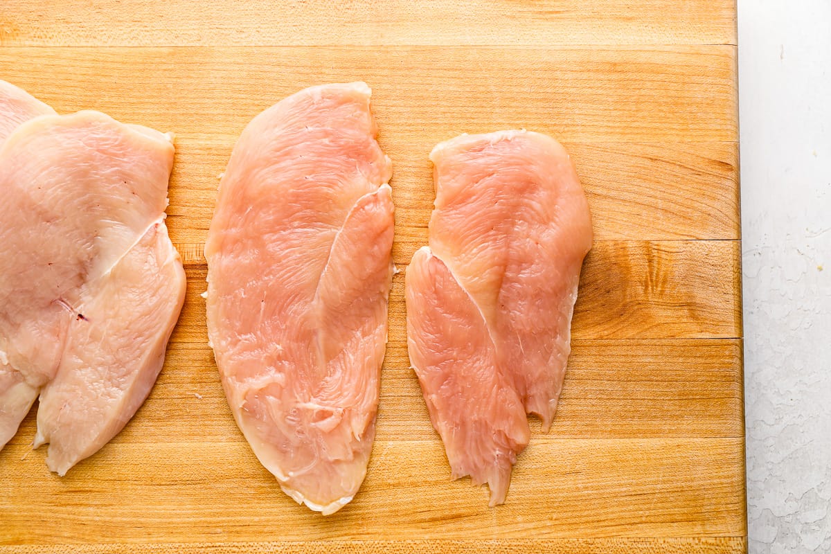 four chicken breasts on a cutting board.