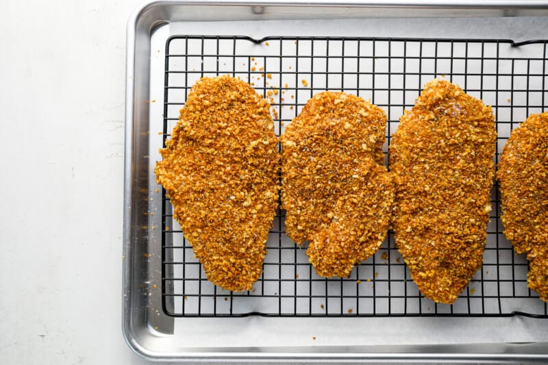 four fried chicken breasts on a cooling rack.