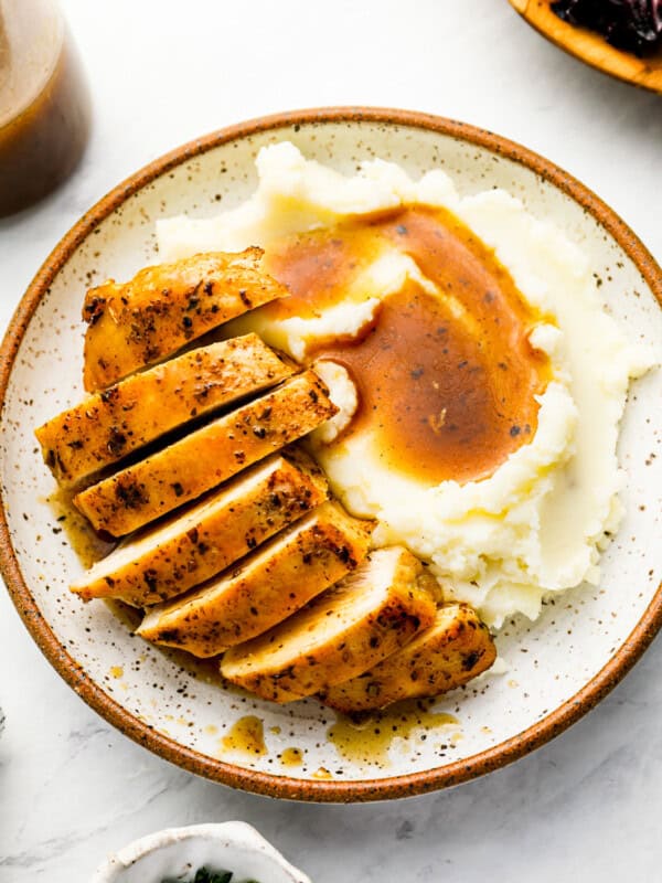 overhead view of a sliced instant pot chicken breas on a white plate with mashed potatoes and gravy.