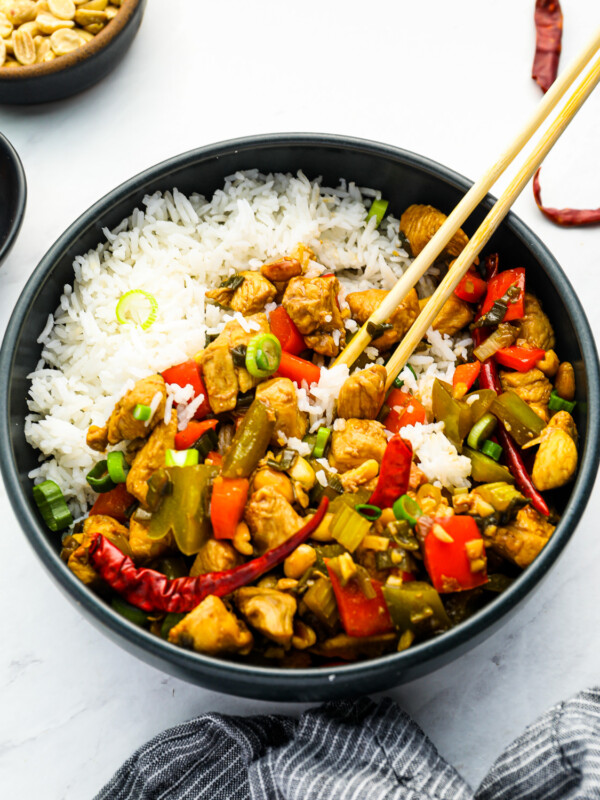 chinese chicken stir fry in a black bowl with rice and chopsticks.