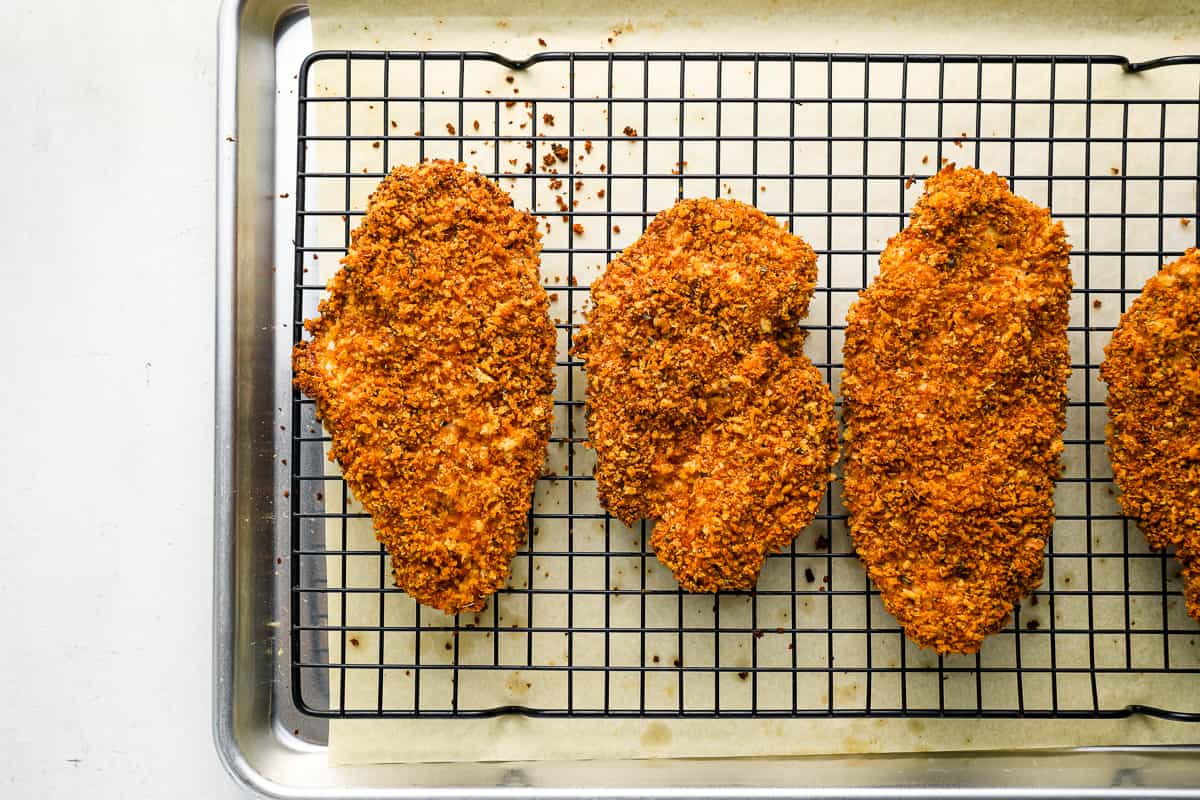 four breaded chicken breasts on a cooling rack.