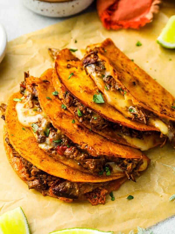 three-quarters view of 4 quesabirria tacos leaning against one another on parchment paper with the filling showing.