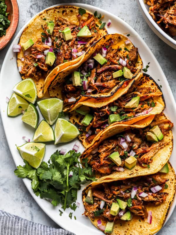 overhead view of 5 carnitas tacos on a white oval serving platter with limes.