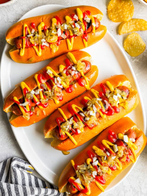 overhead view of 4 topped hot dogs on a white plate.