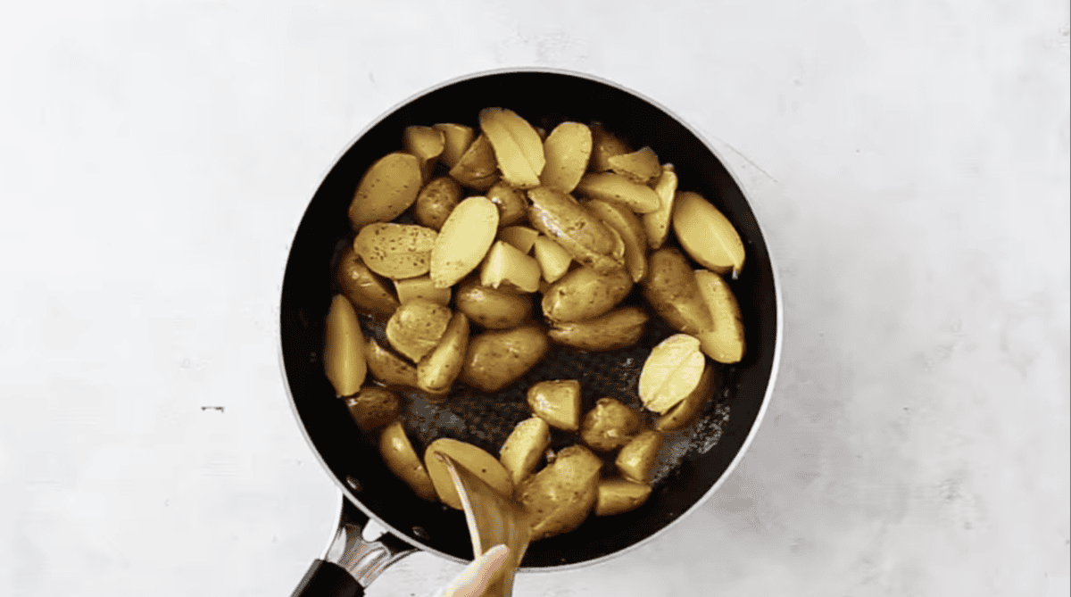 searing potatoes in a pan with a wooden spatula.
