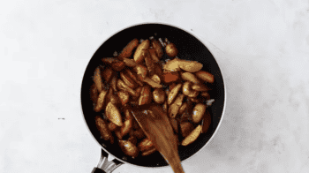 seasoned home fries in a pan with a wooden spatula.
