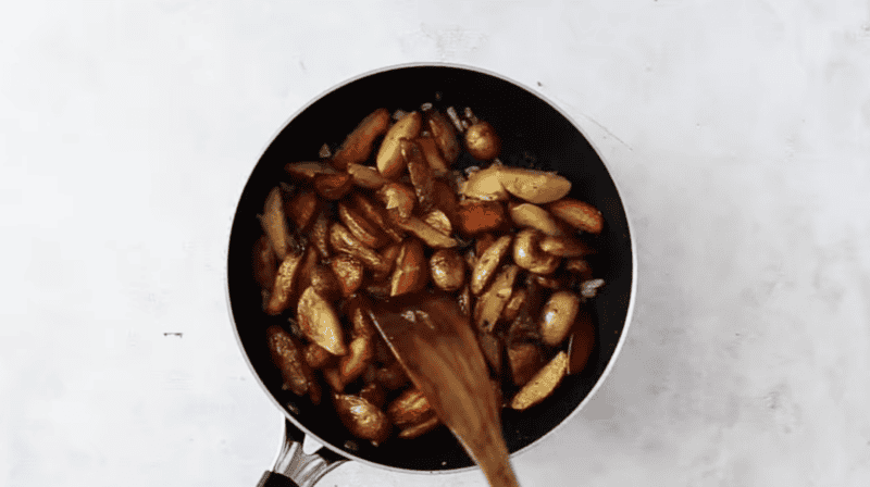 seasoned home fries in a pan with a wooden spatula.