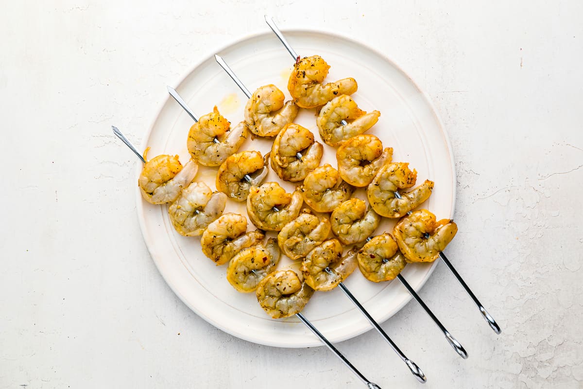 overhead view of 4 raw marinated shrimp skewers on a white plate.