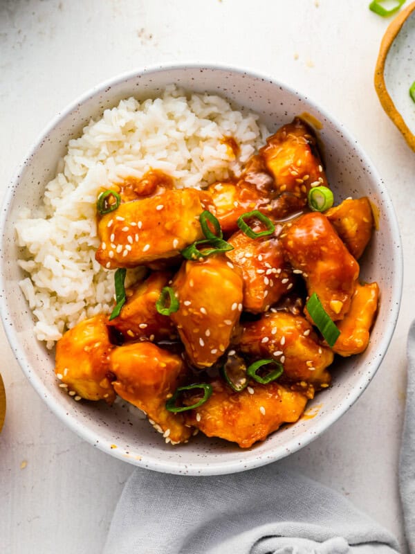 a bowl of asian chicken with rice and sesame seeds.