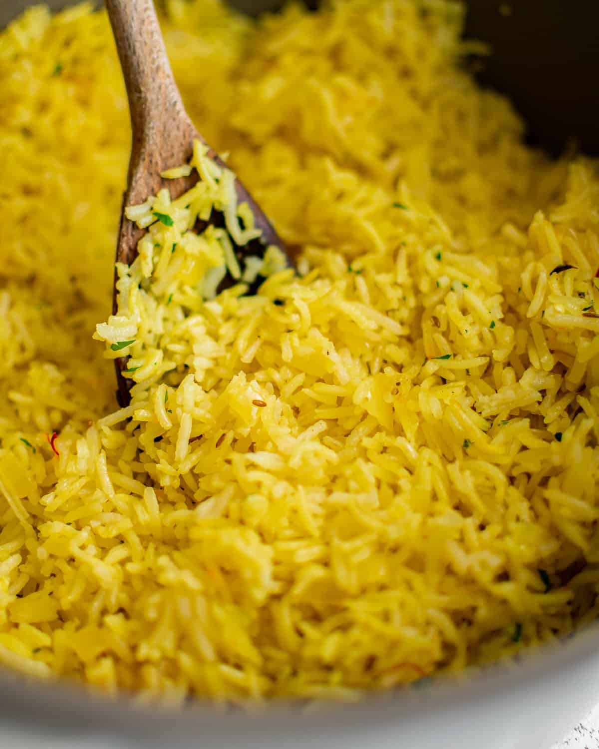 yellow basmati rice in a pan with a wooden spoon.