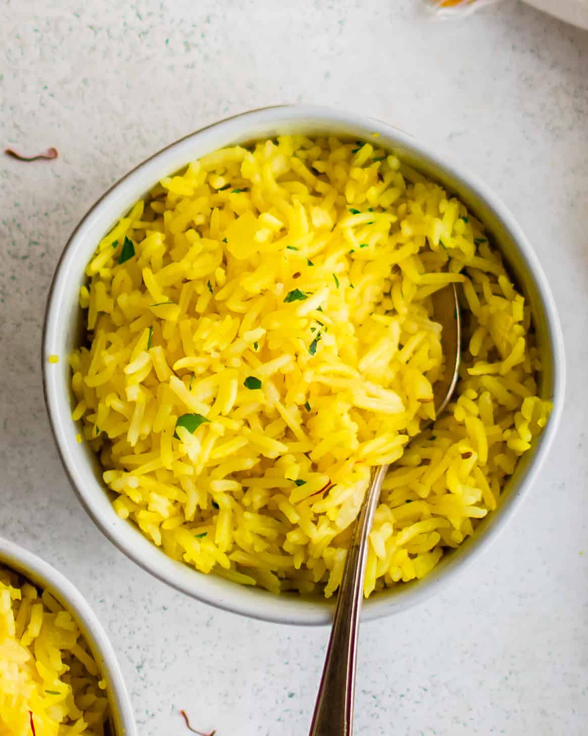 two bowls of yellow saffron rice with a spoon.