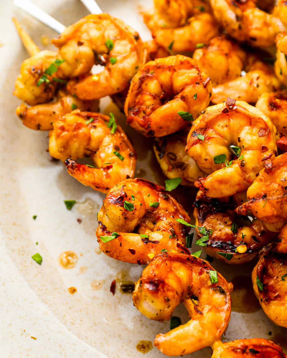 close-up three-quarters view of marinated grilled shrimp skewers on a white plate.