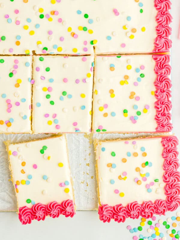 close up overhead view of a partially sliced vanilla cake decorated with white icing with a pink border and sprinkles.