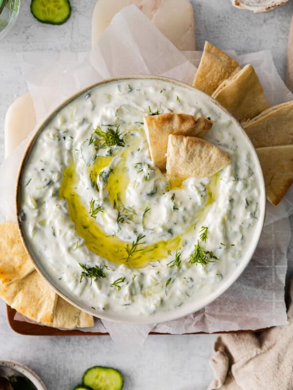 overhead view of tzatziki dip in a white bowl with a drizzle of olive oil and pita chips.