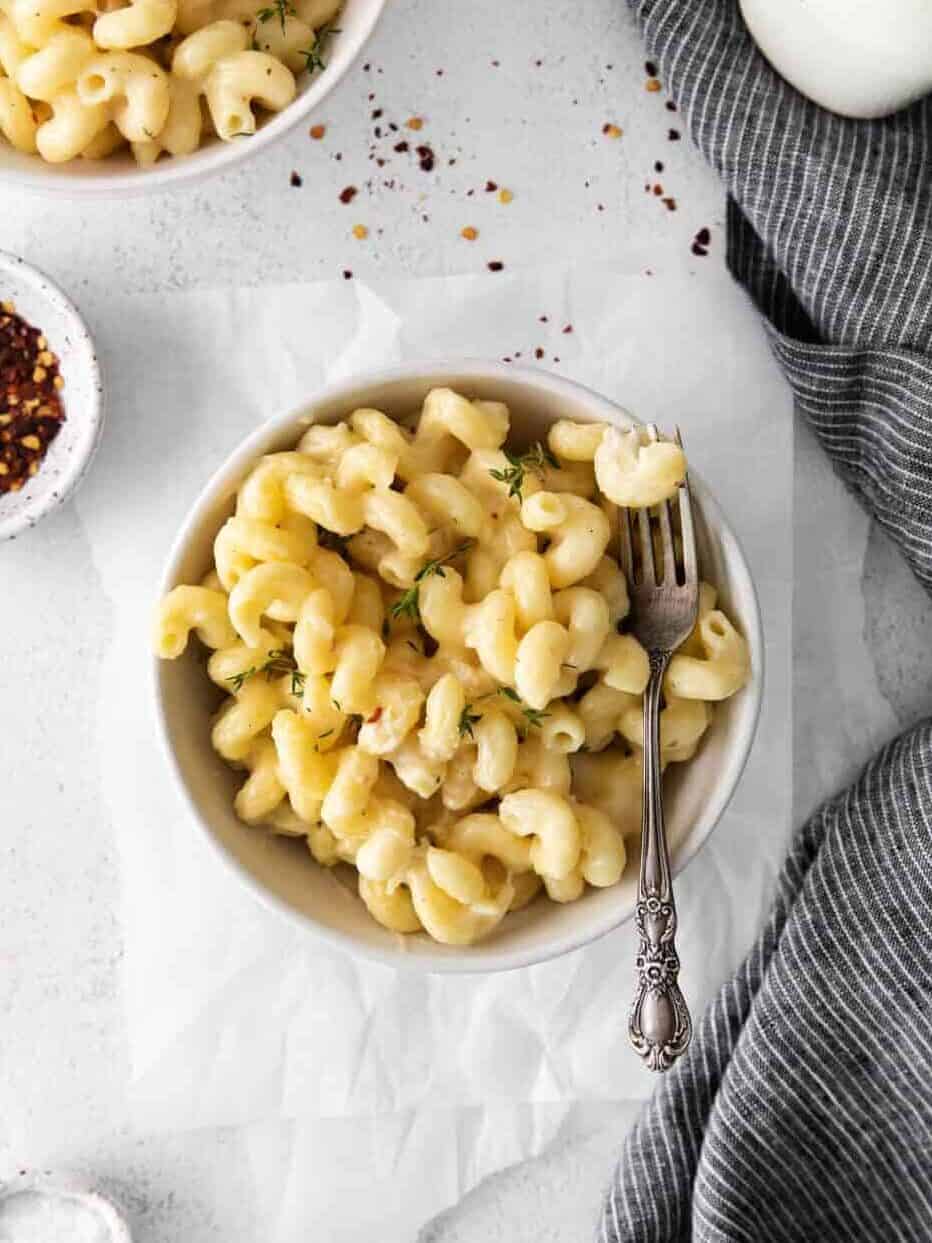 overhead view of a serving of white cheddar mac and cheese in a white bowl with a fork.