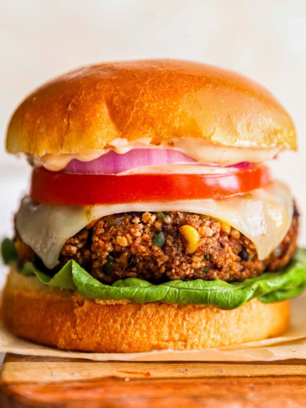 a burger with lettuce, tomato and onion on a wooden cutting board.