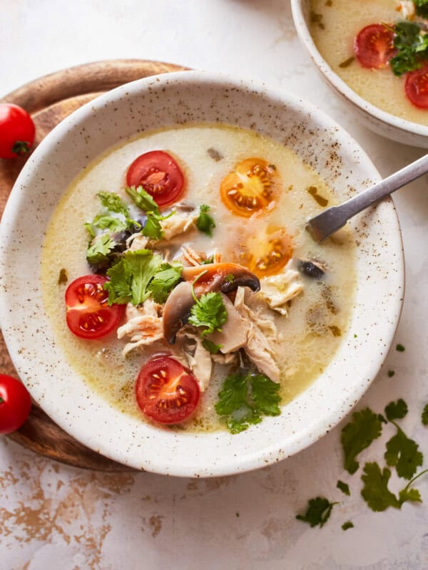 overhead view of a serving of Thai coconut chicken soup in a white bowl with a spoon.