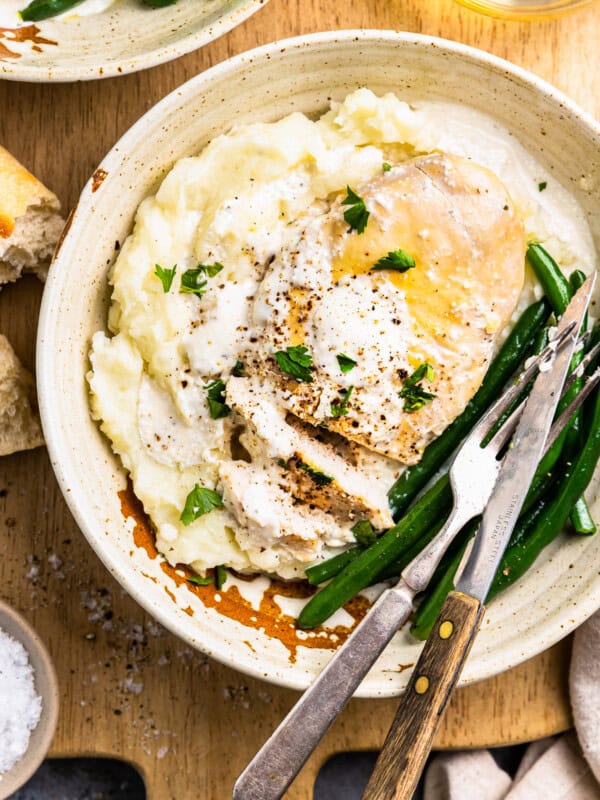 close-up overhead view of crockpot ranch chicken on a white plate with green beans, mashed potatoes, and a fork and knife.